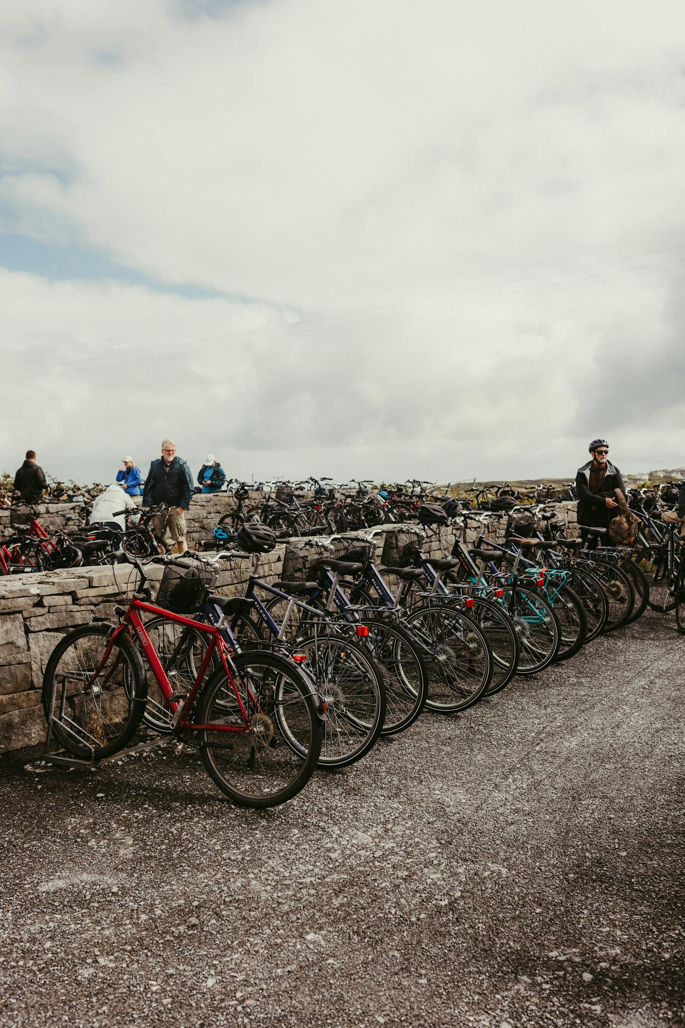 A line of bicycles parked against a stone wall on Inishmore, Ireland, under cloudy skies.